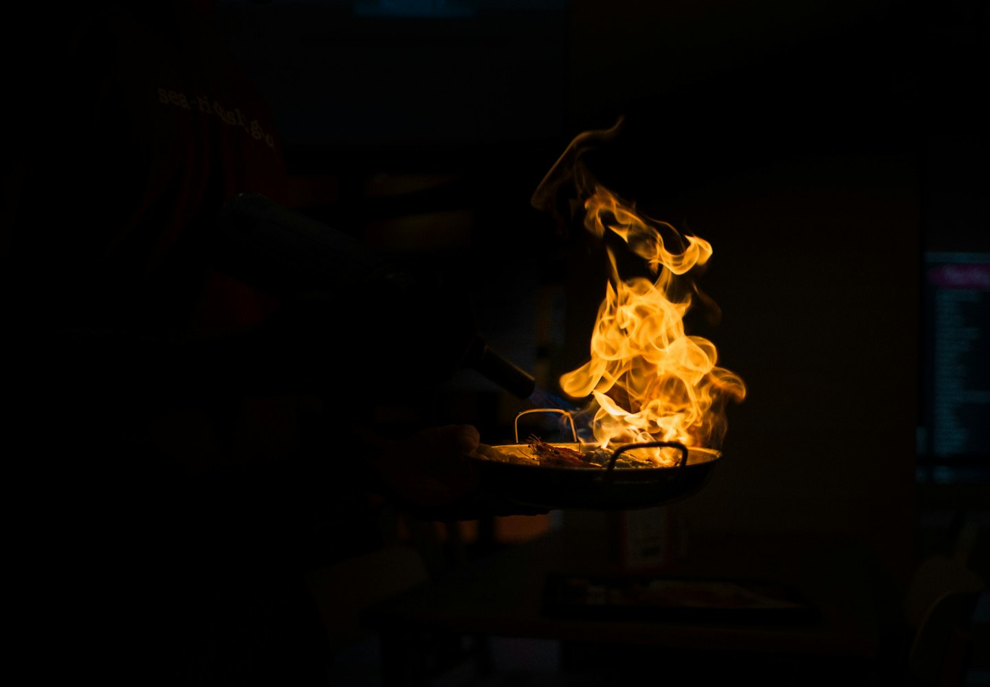 Chef flambéing food in a pan with a torch.